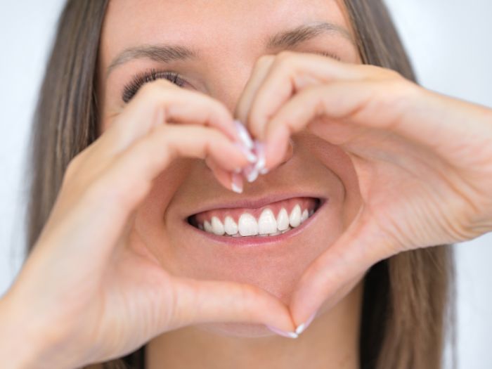 woman holding heart shaped hands near healthy teeth